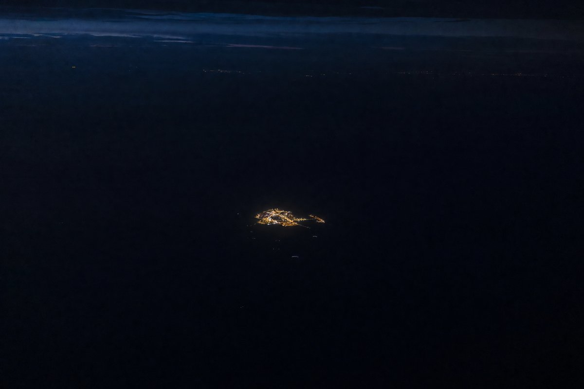 A lone city glowing in darkness surrounded by ocean